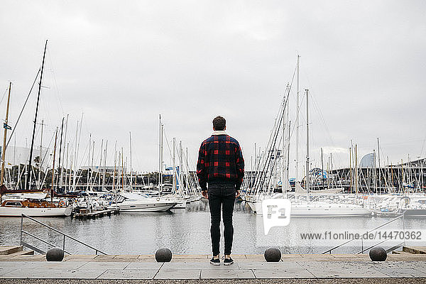 Rückenansicht eines jungen Mannes in legerer Kleidung beim Blick auf den Hafen