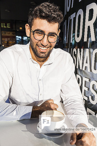 Porträt eines lachenden jungen Geschäftsmannes  der im Straßencafé Kaffee trinkt