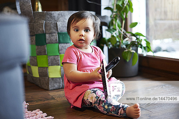 Portrait of cute baby girl sitting on the floor at home holding remote control