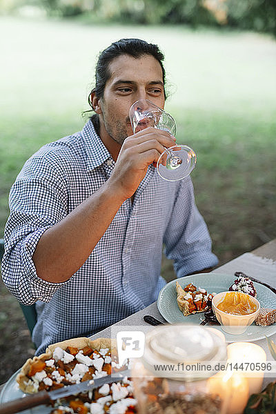 Man drinking glass of wine at garden table