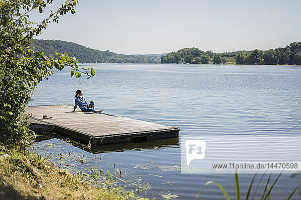 Eine reife Frau sitzt auf einem Steg an einem See und macht eine Pause