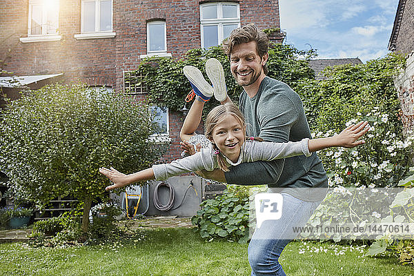 Glücklicher Vater spielt mit Tochter im Garten ihres Hauses