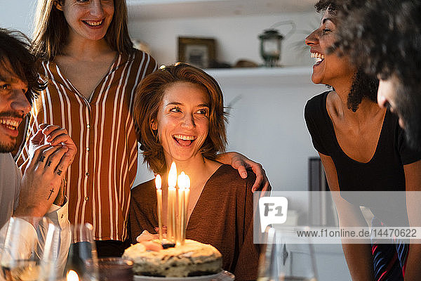 Freunde überraschen junge Frau mit einem Geburtstagskuchen mit brennenden Kerzen