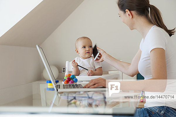 Mother working with little daughter playing at table at home