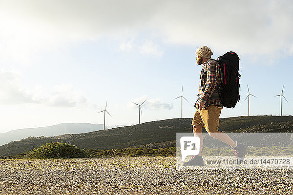 Spanien  Andalusien  Tarifa  Mann auf einer Wanderung auf einem Feldweg mit Windturbinen im Hintergrund