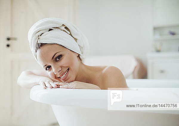 Porträt einer lächelnden Frau mit einem Handtuch um den Kopf  die zu Hause ein Bad nimmt