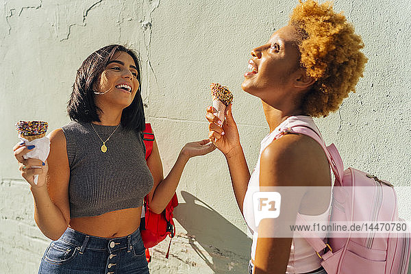 Two happy female friends with ice cream cones at a wall