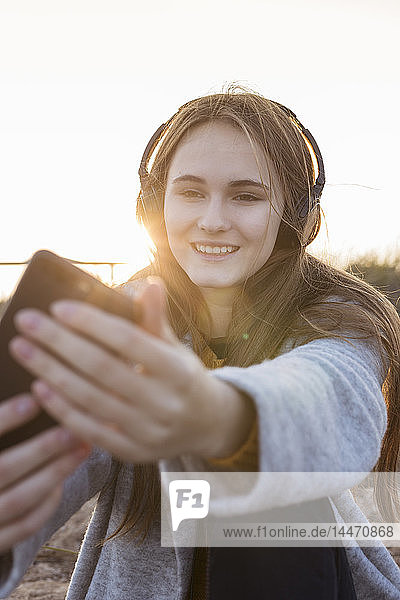 Glückliche junge Frau  die bei Sonnenuntergang beim Musikhören ein Selfie macht