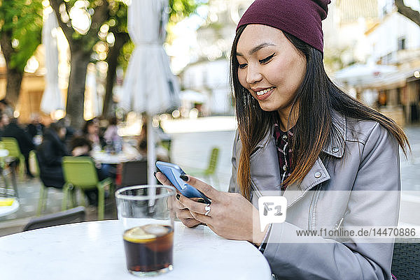 Lächelnde junge Frau mit Smartphone im Straßencafé