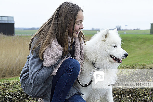 Lächelndes Mädchen  das neben seinem Hund auf einer Wiese kauert