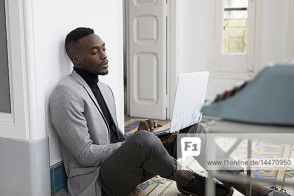 Porträt eines jungen Geschäftsmannes  der im Büro auf dem Boden sitzt und am Laptop arbeitet