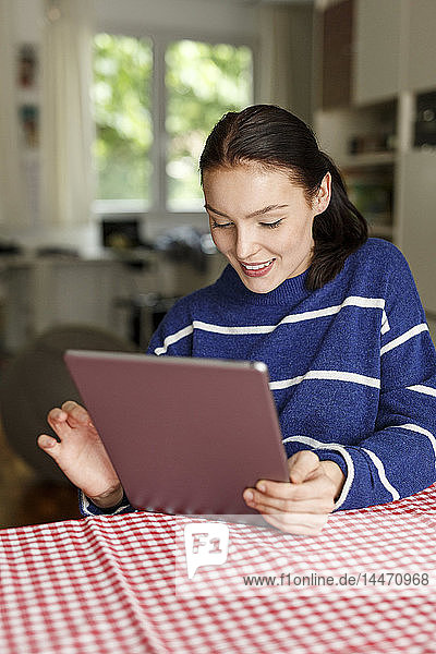 Junge Frau sitzt zu Hause und benutzt ein digitales Tablett
