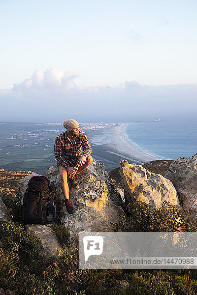 Spanien  Andalusien  Tarifa  Mann auf einer Wanderung an der Küste auf einem Felsen sitzend