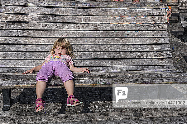 Sweden  girl lying on wooden bench on town square