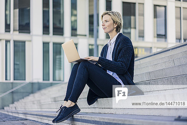 Junge Geschäftsfrau sitzt auf einer Treppe und benutzt einen Laptop