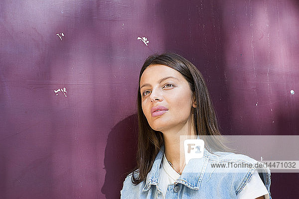 Porträt einer tagträumenden jungen Frau vor violettem Hintergrund