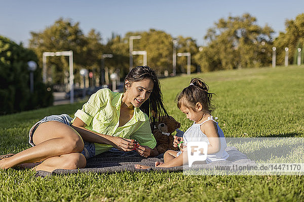 Happy mother playing with daughter on a blanket in park