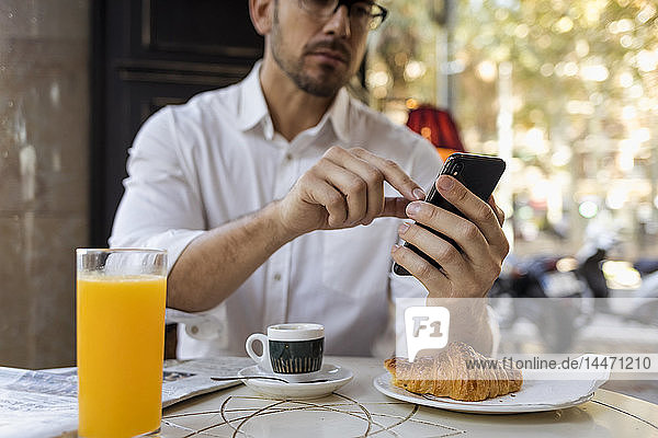 Geschäftsmann frühstückt in einem Cafe und benutzt sein Handy