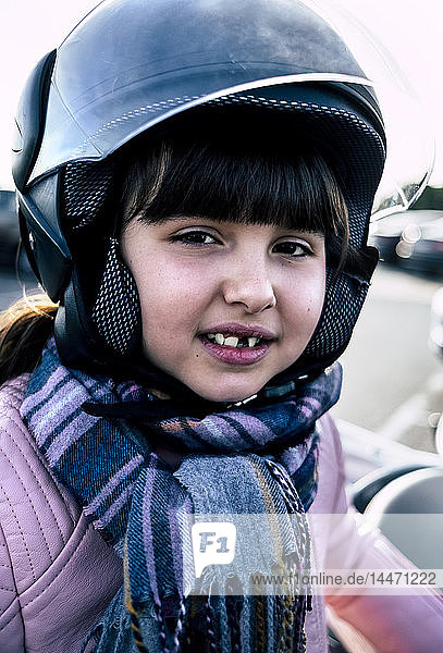 Porträt eines kleinen Mädchens mit Zahnlücke mit Helm auf Motorrad