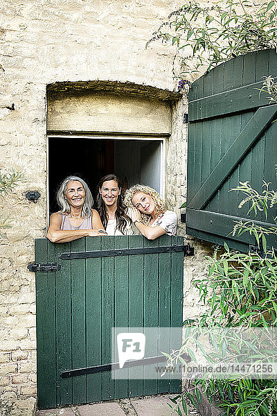 Porträt von drei lächelnden Frauen unterschiedlichen Alters hinter einem stabilen Tor