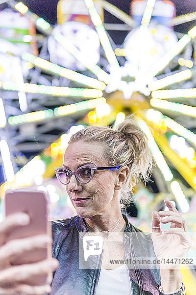 Portrait of mature woman taking selfie in front of big wheel at fair