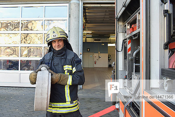 Portrait of firefighter at fire engine holding firehose