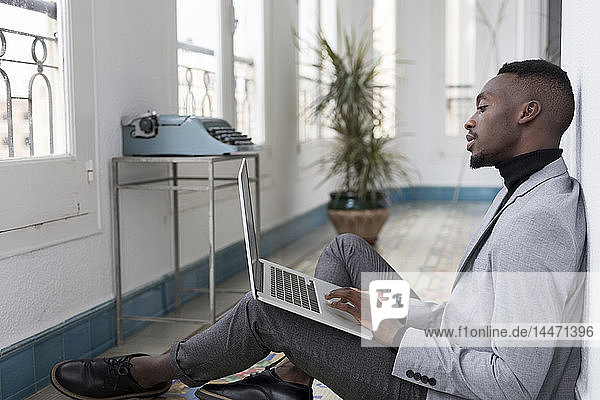 Young businessman sitting on floor in the office working on laptop