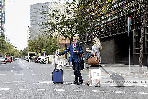 Leitender Geschäftsmann und Geschäftsfrau mit Gepäck beim Überqueren der Straße in der Stadt