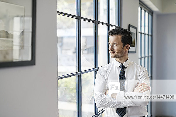 Confident businessman standing in office looking out of window