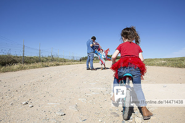 Girl with bicycle and man with American flag on path in remote landscape