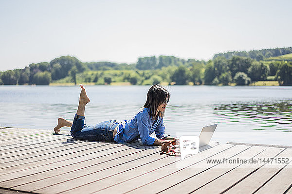 Mature woman working at a lake  using laptop on a jetty