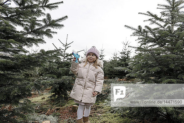 Glückliches Mädchen spielt mit Wasserpistole auf einer Weihnachtsbaumplantage