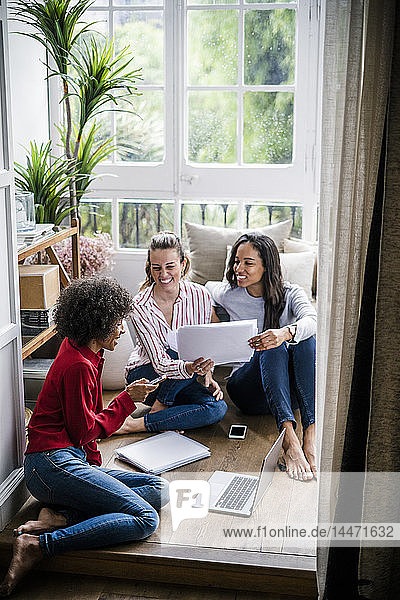 Drei Frauen mit Laptop  Handy und Dokumenten  die zu Hause auf dem Boden sitzen