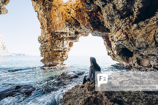 Spanien  Alicante  Frau sitzt auf den Felsen am Strand von Benitachell