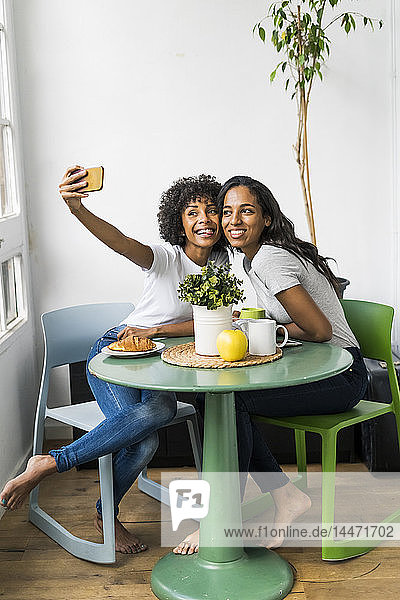 Zwei glückliche Freundinnen sitzen am Tisch und machen ein Selfie