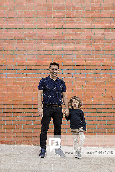Porträt von Vater und Sohn stehen Hand in Hand an einer Ziegelmauer