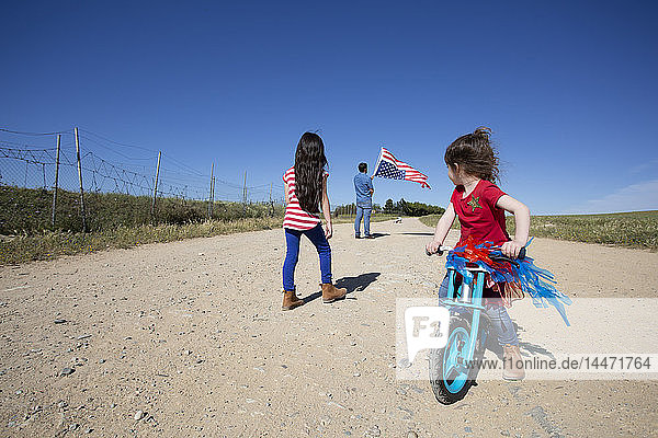 Mädchen mit Fahrrad und Mann mit amerikanischer Flagge auf Weg in entlegener Landschaft