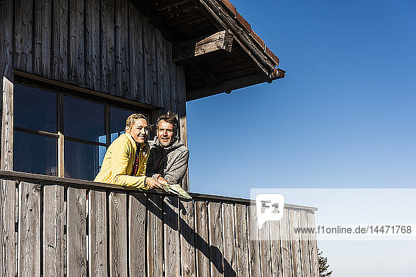 Paar lehnt auf dem Balkon einer Berghütte  hält Karte