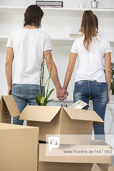 Paar mit Pappkartons steht Hand in Hand im neuen Zuhause