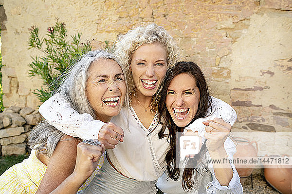 Porträt von drei aufgeregten Frauen unterschiedlichen Alters  die sich umarmen und anfeuern