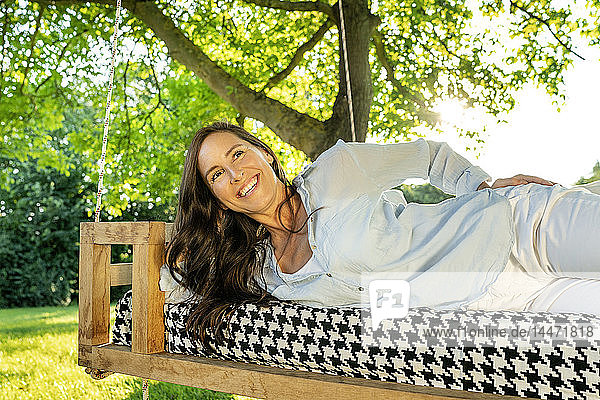 Reife Frau entspannt sich auf einem hängenden Bett im Garten