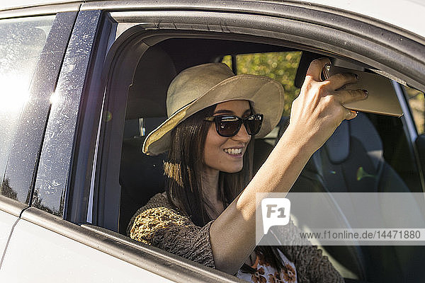 Lächelnde junge Frau sitzt in einem Auto und nimmt Selfie mit Handy
