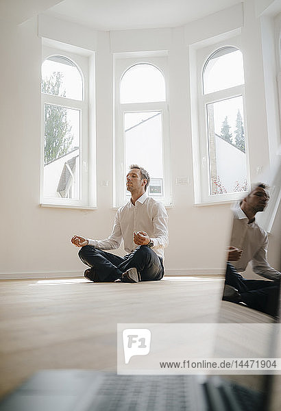 Geschäftsmann in frisch renoviertem Haus  im Schneidersitz auf dem Boden sitzend  meditierend  mit Laptop im Vordergrund