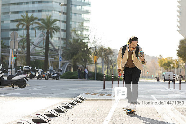 Mann betrachtet Handy beim Skateboarden in der Stadt