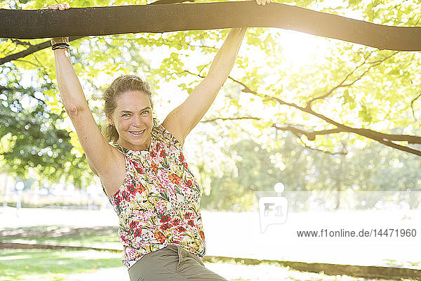 Porträt einer lächelnden reifen Frau in einem Top mit Blumenmuster  die sich in einem Park vergnügt
