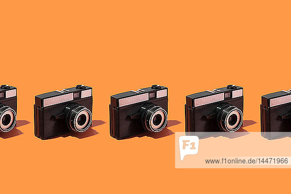 Plastik-Fotokameras in einer Reihe auf orangem Hintergrund