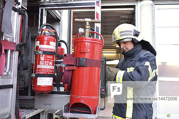 Firefighter standing at fire engine with fire extinguisher