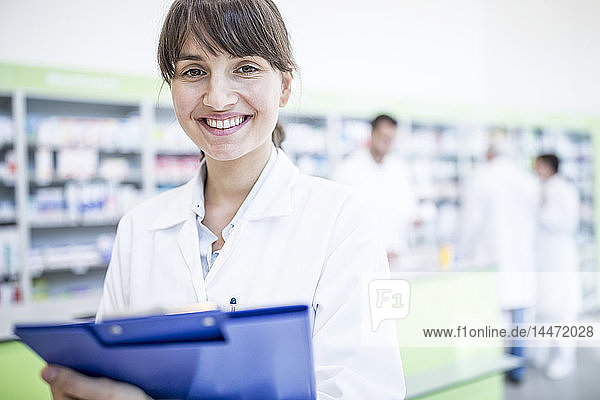 Portrait of smiling pharmacist in pharmacy holding clipboard