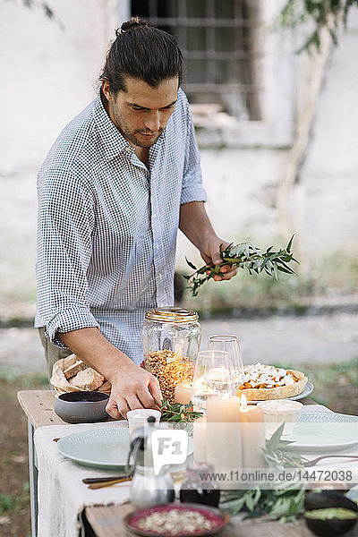 Mann bereitet ein romantisches Essen bei Kerzenlicht im Freien zu