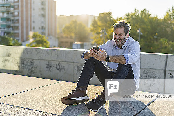 Smiling mature man sitting in the city using cell phone